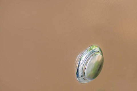 Closeup of silver metallic push button switch used to turn on power to machine on soft brown