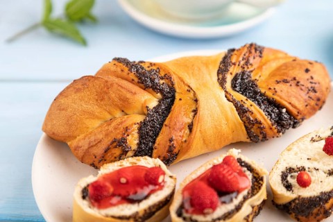 Homemade sweet bun with strawberry jam and cup of green tea on a blue wooden background. side view,