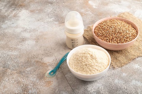 Powdered milk and buckwheat baby food mix, infant formula, pacifier, bottle, spoon on brown