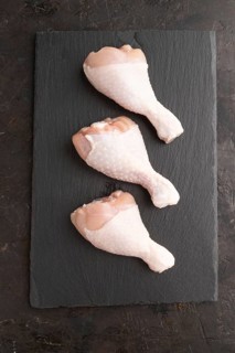 Raw chicken legs on a black slate cutting board on a black concrete background. Top view, flat lay,