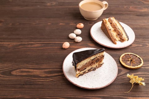 Chocolate biscuit cake with caramel cream, cup of coffee on brown wooden background. side view,