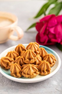 Homemade soft caramel fudge candies on blue plate and cup of coffee on gray concrete background,