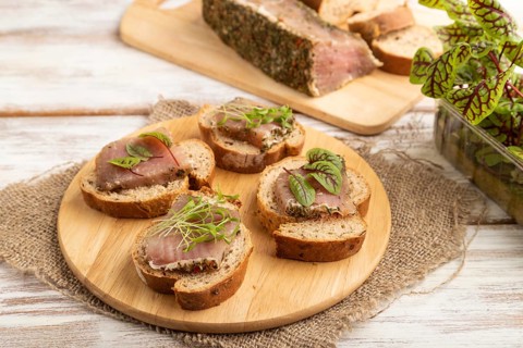 Bread sandwiches with jerky salted meat, sorrel and cilantro microgreen on white wooden background