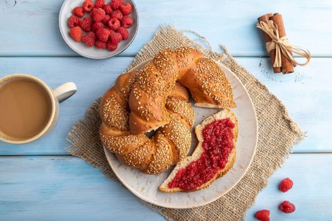 Homemade sweet bun with raspberry jam and cup of coffee on a blue wooden background and linen