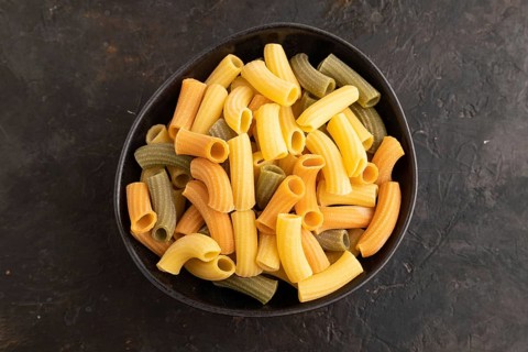 Rigatoni colored raw pasta with tomato, eggs, spices, herbs on black concrete background. Top view,
