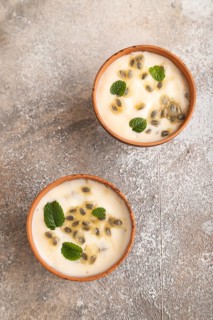 Yoghurt with granadilla and mint in clay bowl on brown concrete background. top view, flat lay,
