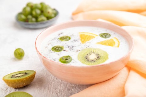 Yogurt with kiwi, gooseberry, chia in ceramic bowl on gray concrete background and orange linen
