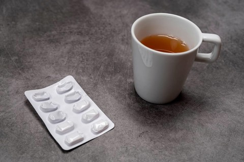 A blister pack with pills next to a cup of tea on a grey background, top view, studio shot,