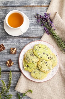 Green cookies with chocolate and mint on ceramic plate with cup of green tea and linen textile on