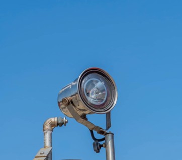 Searchlight with cracked lens mounted on pole against blue sky