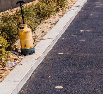Plastic industrial spray bottle sitting on the curb of parking lot with black asphalt paving and a
