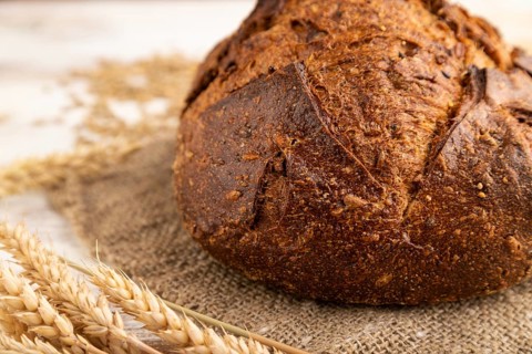 Fresh homemade golden grain bread with ears of wheat and rye on white wooden background and linen