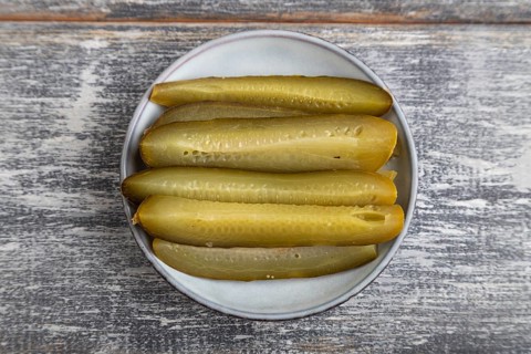 Marinated cucumber on a blue ceramic plate on a gray wooden background. Top view, flat lay, close