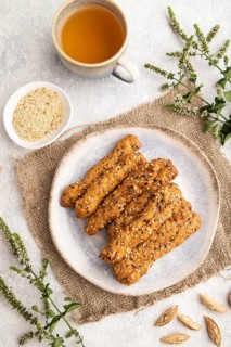 Crumble cookies with seasme and almonds on ceramic plate with cup of green tea and linen textile on