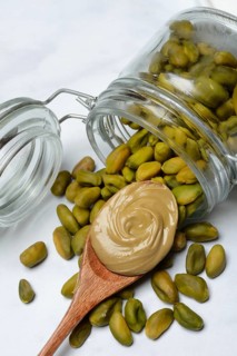 Pistachios with glass container and spoon with pistachio cream, pistachio