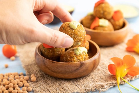 Falafel with guacamole on blue wooden background and linen textile with hand. Side view, close up,