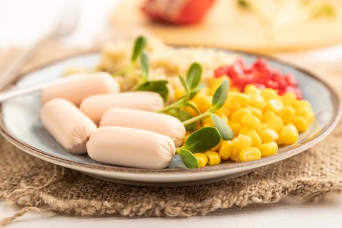Mixed quinoa porridge, sweet corn, pomegranate seeds and small sausages on white wooden background.