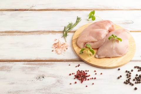 Raw chicken breast with herbs and spices on a wooden cutting board on a white wooden background.