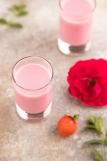 Sweet strawberry liqueur in glass on a gray concrete background and orange textile. side view,