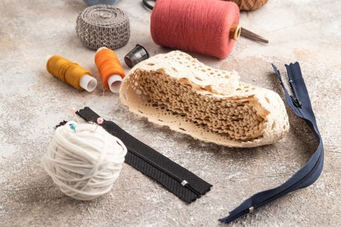 Sewing accessories: scissors, thread, thimbles, braid on brown concrete background. Side view,