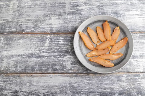 Salted meat on a wooden plate on a gray wooden background. Top view, flat lay, close up, copy space