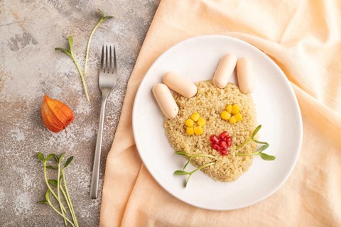 Funny mixed quinoa porridge, sweet corn, pomegranate seeds and small sausages in form of cat face