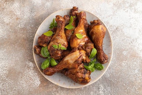 Smoked chicken legs with herbs and spices on a ceramic plate on a brown concrete background. Top