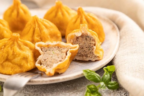 Fried manti dumplings with pepper, basil on gray concrete background and linen textile. Side view,