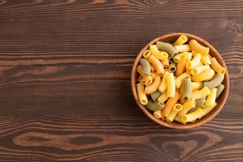 Rigatoni colored raw pasta with tomato, eggs, spices, herbs on brown wooden background. Top view,