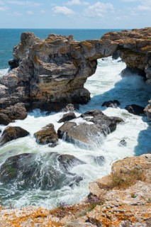 A natural rock arch on a rough coast with waves crashing against rocks, rock arch, stone arch,
