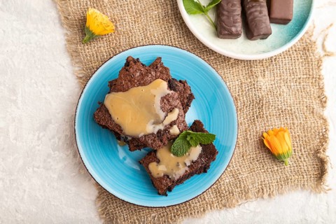 Chocolate brownie with caramel sauce with a cup of coffee on gray concrete background and linen