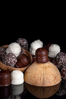 Stack of different chocolate kisses on a dark background, coconut half, reflection, copy space