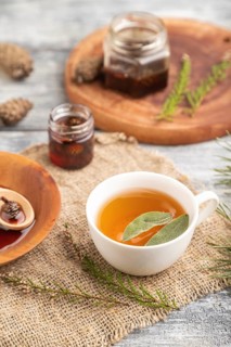 Pine cone jam with herbal tea on gray wooden background and linen textile. Side view, close up,