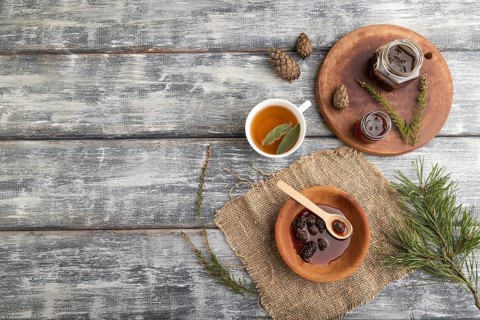 Pine cone jam with herbal tea on gray wooden background and linen textile. Top view, flat lay, copy