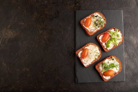 Red beet bread sandwiches with cream cheese, tomatoes and microgreen on black concrete background.