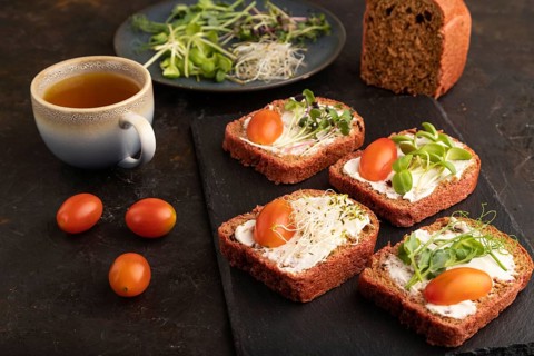 Red beet bread sandwiches with cream cheese, tomatoes and microgreen on black concrete background.