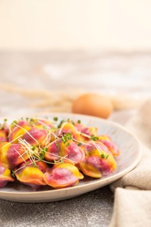 Rainbow colored dumplings with pepper, herbs, microgreen on brown concrete background and linen