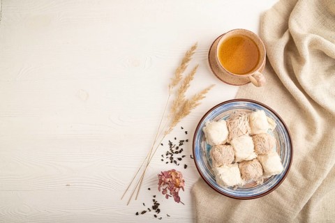 Traditional arabic sweets pishmanie and a cup of green tea on white wooden background and linen