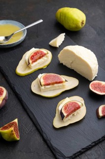 Summer appetizer with pear, cottage cheese, figs and honey on slate board on a black concrete
