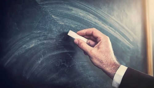 Closeup teacher hand holding a piece of chalk starts writing on the blank blackboard. Businessman