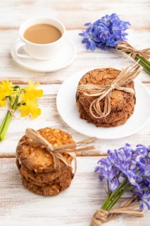 Oatmeal cookies with spring snowdrop flowers bluebells, narcissus and cup of coffee on white wooden