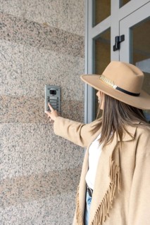 Vertical Side view of unrecognizable woman wearing a hat pushing the button of the intercom of