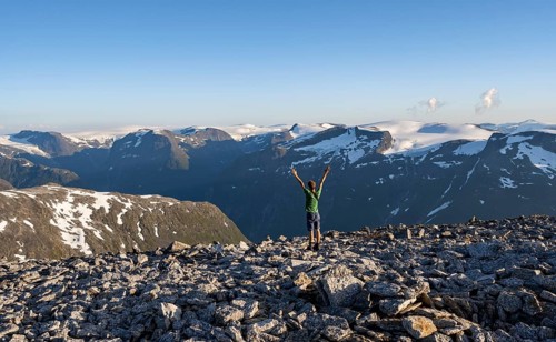Mountain panorama with mountain peaks and Jostedalsbreen glacier, mountaineer stretches his arms in