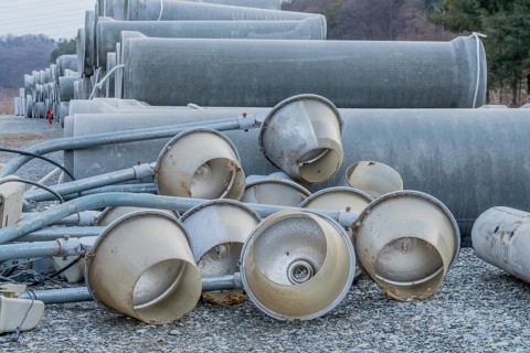 Old dirty street light fixtures laying on gravel in front of culverts at construction site