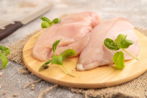 Raw chicken breast with herbs and spices on a wooden cutting board on a brown concrete background.