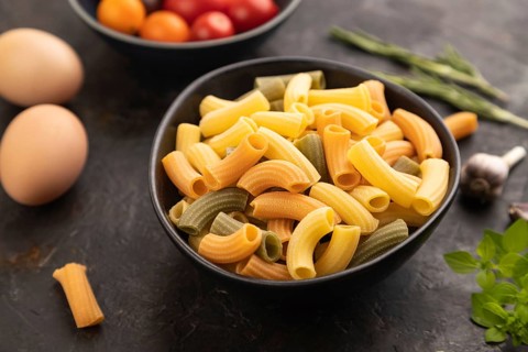 Rigatoni colored raw pasta with tomato, eggs, spices, herbs on black concrete background. Side