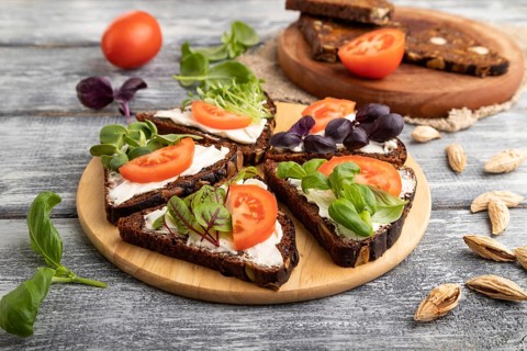 Grain rye bread sandwiches with cream cheese, tomatoes and microgreen on gray wooden background and
