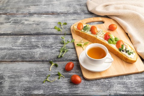 Long white bread sandwich with cream cheese, tomatoes and microgreen on gray wooden background and