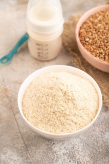 Powdered milk and buckwheat baby food mix, infant formula, pacifier, bottle, spoon on brown