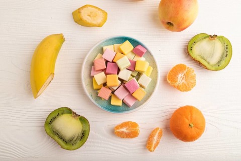Various fruit jelly chewing candies on plate on white wooden background. apple, banana, tangerine,